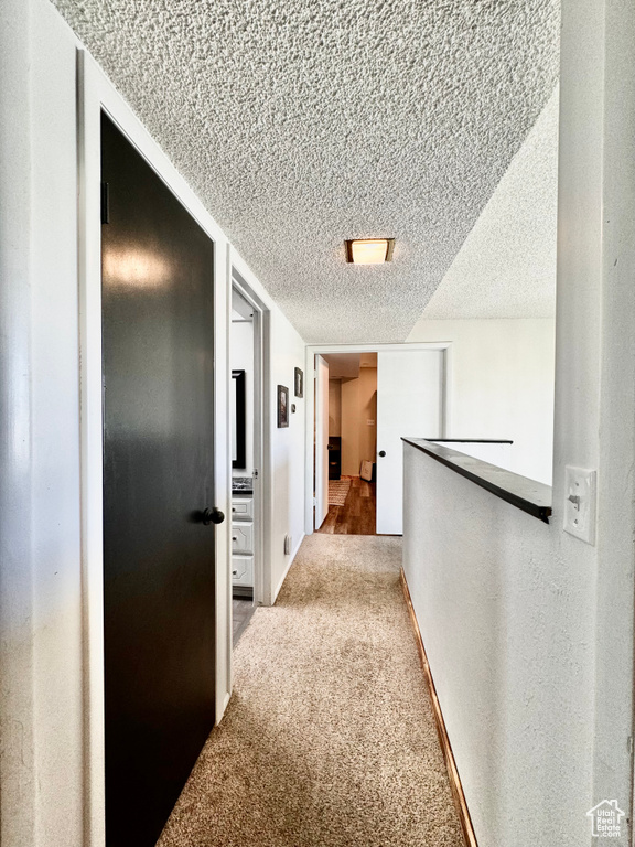 Hall featuring light carpet and a textured ceiling