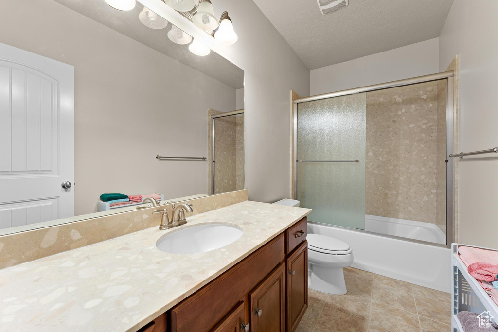 Full bathroom with shower / bath combination with glass door, toilet, vanity, and tile patterned floors