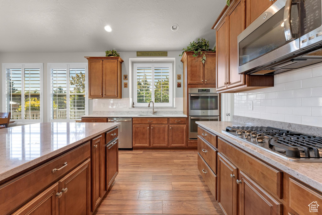 Kitchen with decorative backsplash, a wealth of natural light, light hardwood / wood-style floors, and appliances with stainless steel finishes