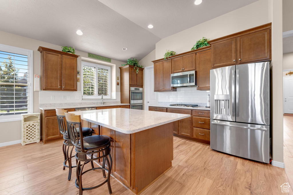 Kitchen featuring lofted ceiling, tasteful backsplash, light hardwood / wood-style flooring, stainless steel appliances, and a center island