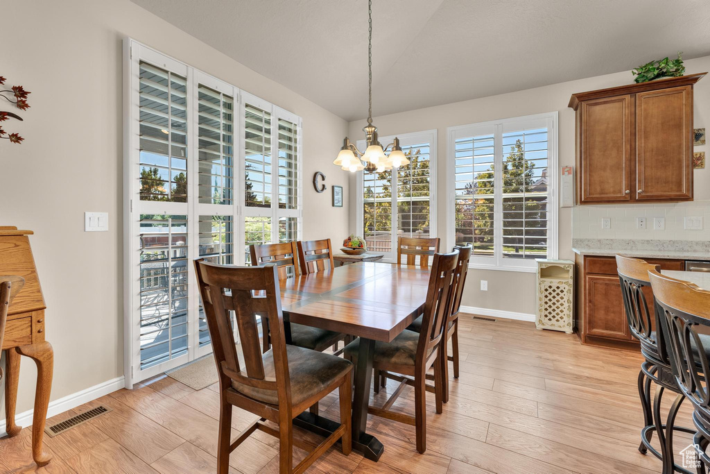 Dining room with light wood-type flooring, vaulted ceiling, and a notable chandelier