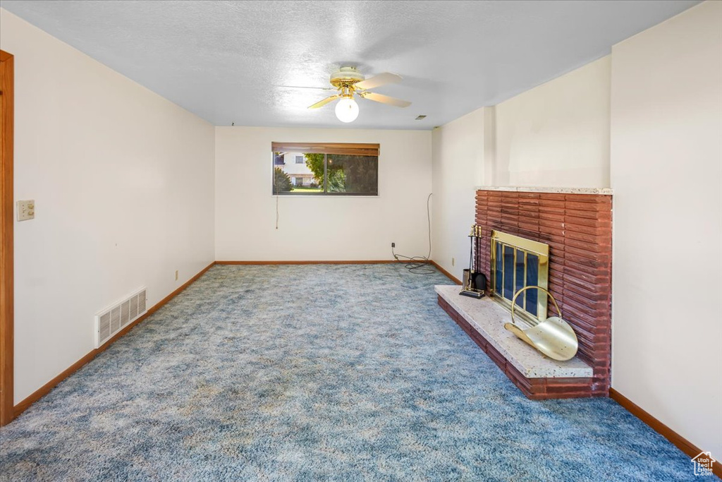 Unfurnished living room featuring carpet, ceiling fan, a fireplace, and a textured ceiling