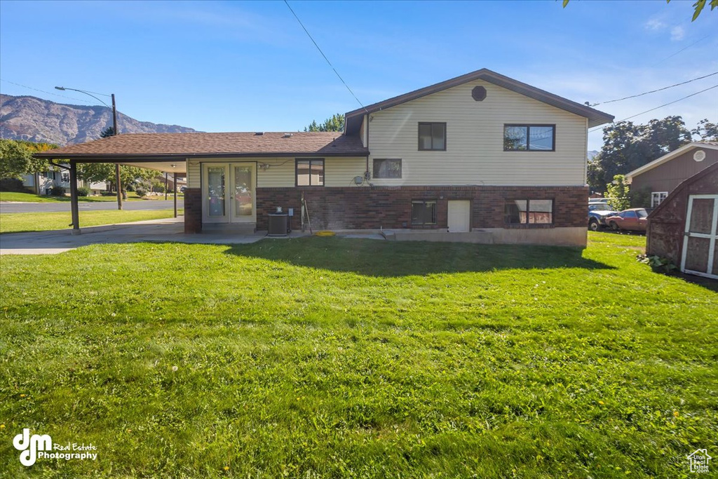 Back of house featuring a mountain view, a carport, a yard, and central air condition unit