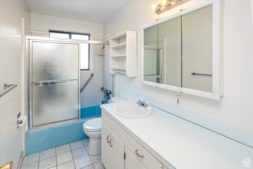 Full bathroom with tile patterned floors, shower / bath combination with glass door, vanity, and toilet