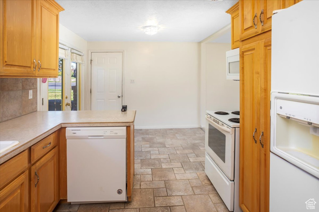 Kitchen with white appliances, kitchen peninsula, and backsplash