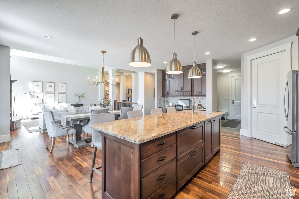 Kitchen with pendant lighting, a kitchen island, a textured ceiling, dark wood-type flooring, and a kitchen breakfast bar