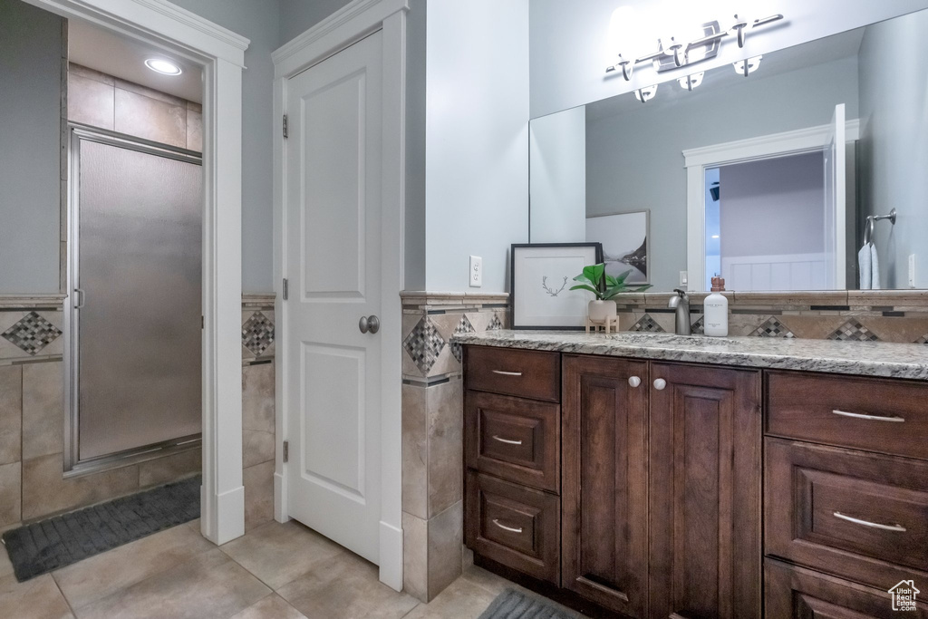 Bathroom featuring tile walls, tile patterned floors, a shower with door, and vanity