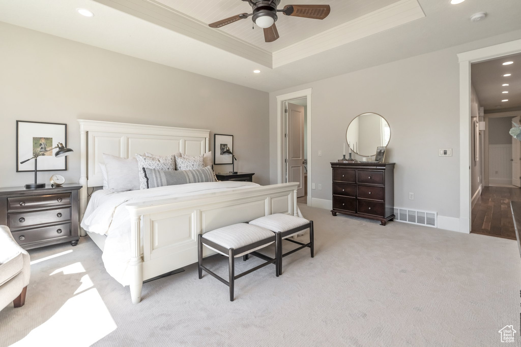 Bedroom with ceiling fan, light colored carpet, a tray ceiling, and ornamental molding