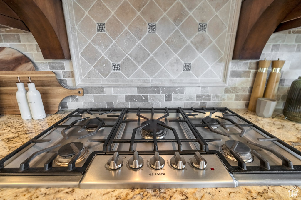 Room details featuring stainless steel gas cooktop, stone counters, and decorative backsplash