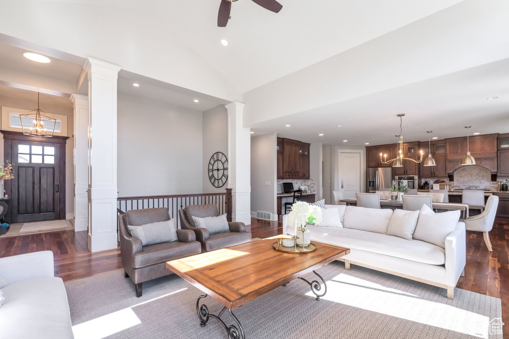 Living room featuring ornate columns, ceiling fan with notable chandelier, dark hardwood / wood-style flooring, and high vaulted ceiling