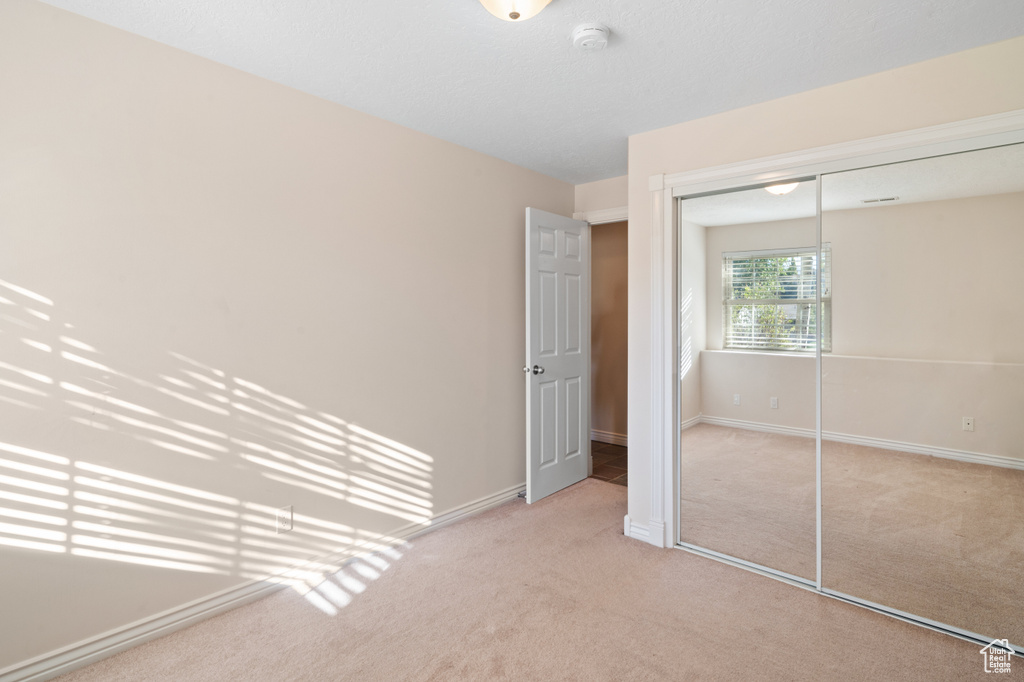 Unfurnished bedroom with light carpet and a closet