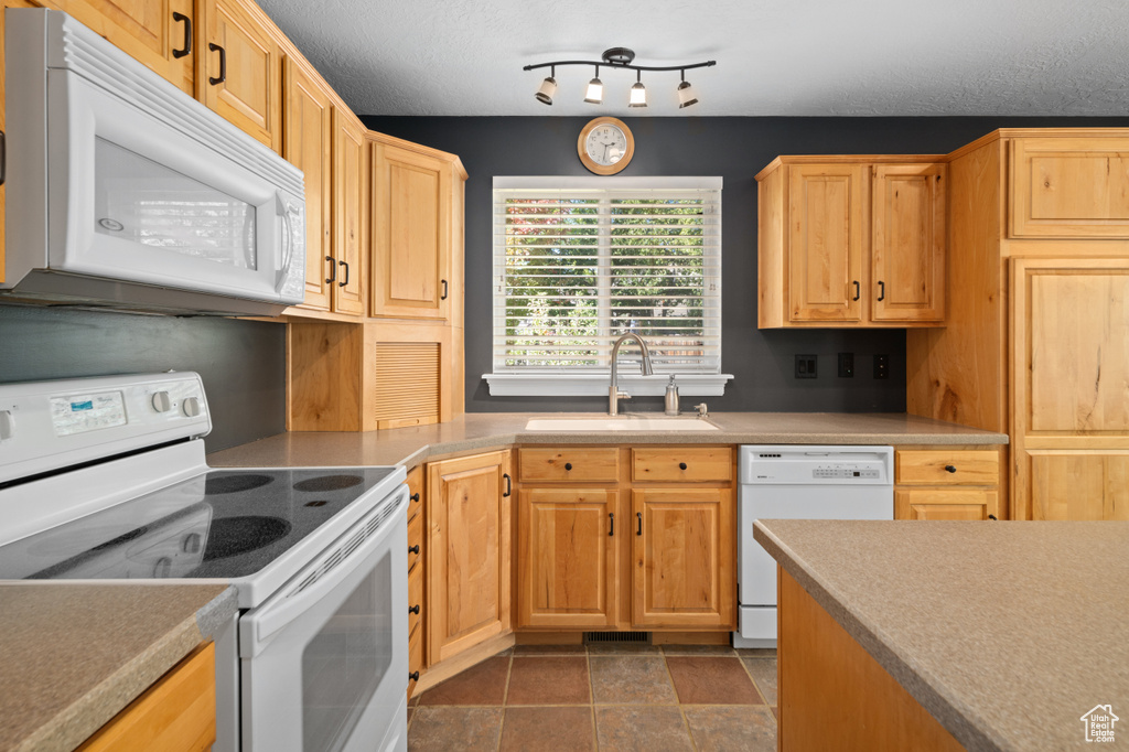 Kitchen with a textured ceiling, light brown cabinetry, white appliances, and sink