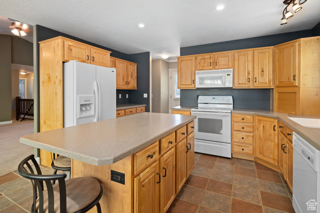 Kitchen featuring light brown cabinetry, a kitchen breakfast bar, white appliances, and a kitchen island