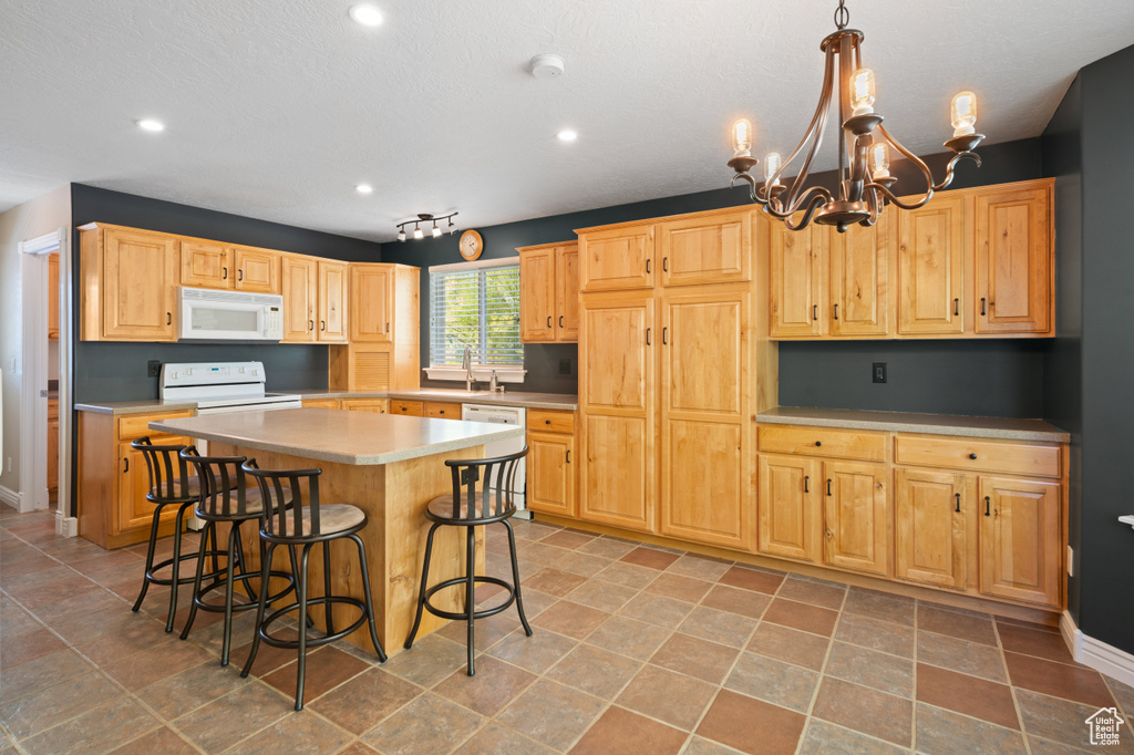 Kitchen with a breakfast bar, a chandelier, a kitchen island, white appliances, and decorative light fixtures