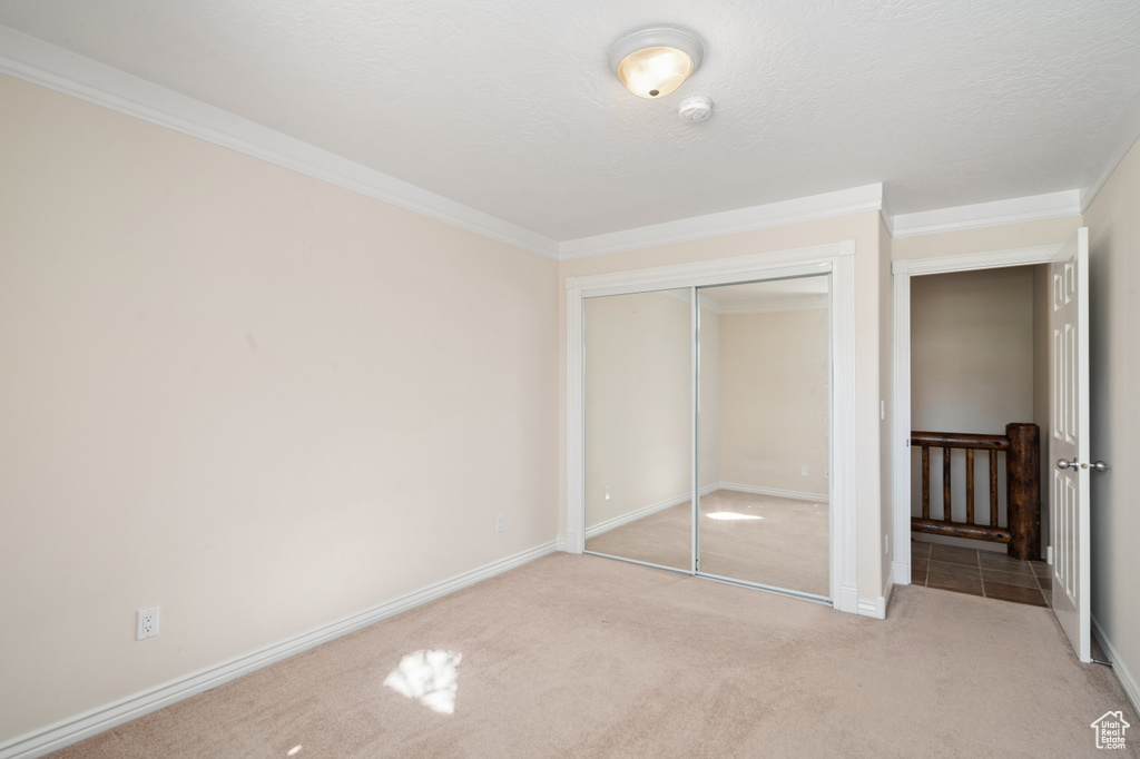 Unfurnished bedroom featuring light carpet, a textured ceiling, a closet, and crown molding