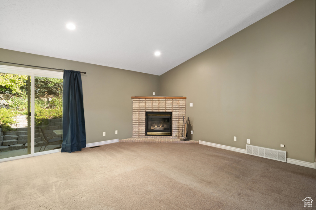 Unfurnished living room featuring a brick fireplace, light carpet, and vaulted ceiling