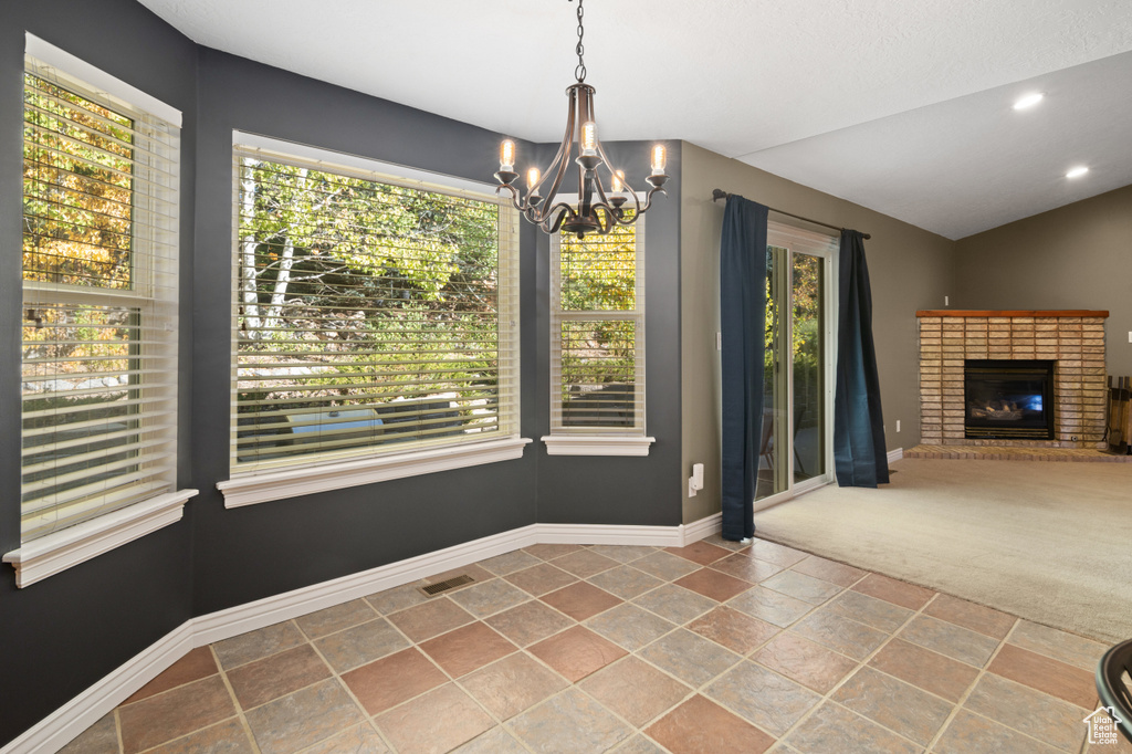 Unfurnished dining area with a brick fireplace, a chandelier, carpet, and a wealth of natural light