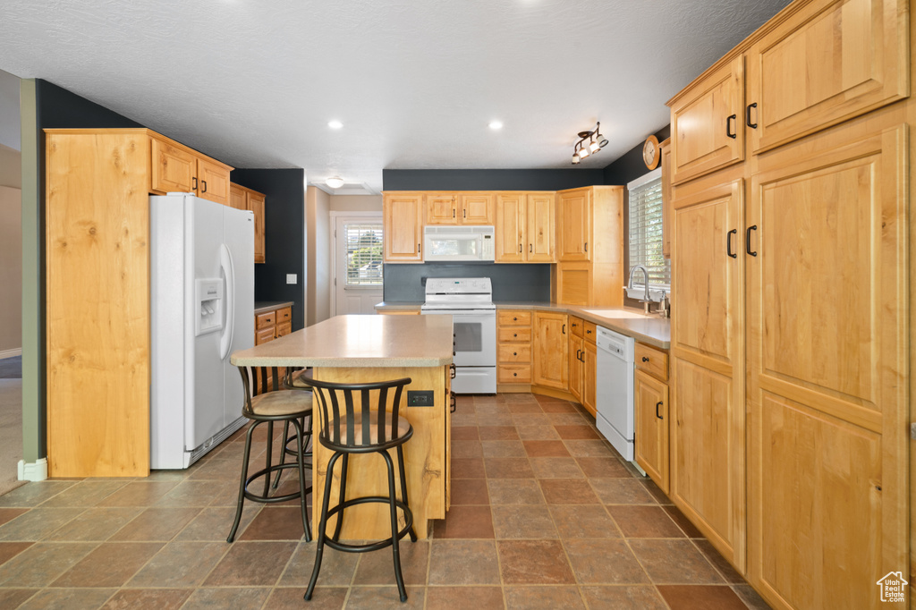 Kitchen featuring light brown cabinets, sink, white appliances, a center island, and a kitchen bar