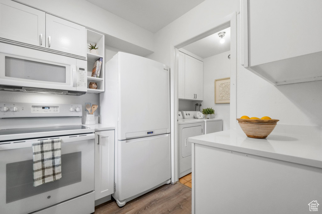 Kitchen with light hardwood / wood-style flooring, white appliances, white cabinetry, and washer and clothes dryer