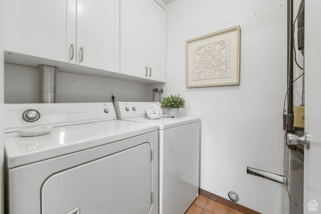 Clothes washing area with cabinets, light tile patterned floors, and washer and dryer