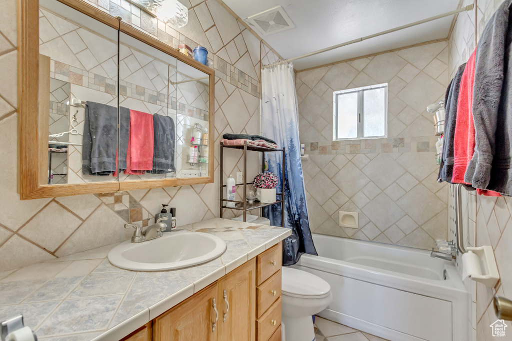 Full bathroom featuring tile walls, shower / bathtub combination with curtain, backsplash, vanity, and toilet