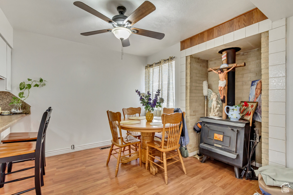 Dining area with a wood stove, light hardwood / wood-style floors, and ceiling fan