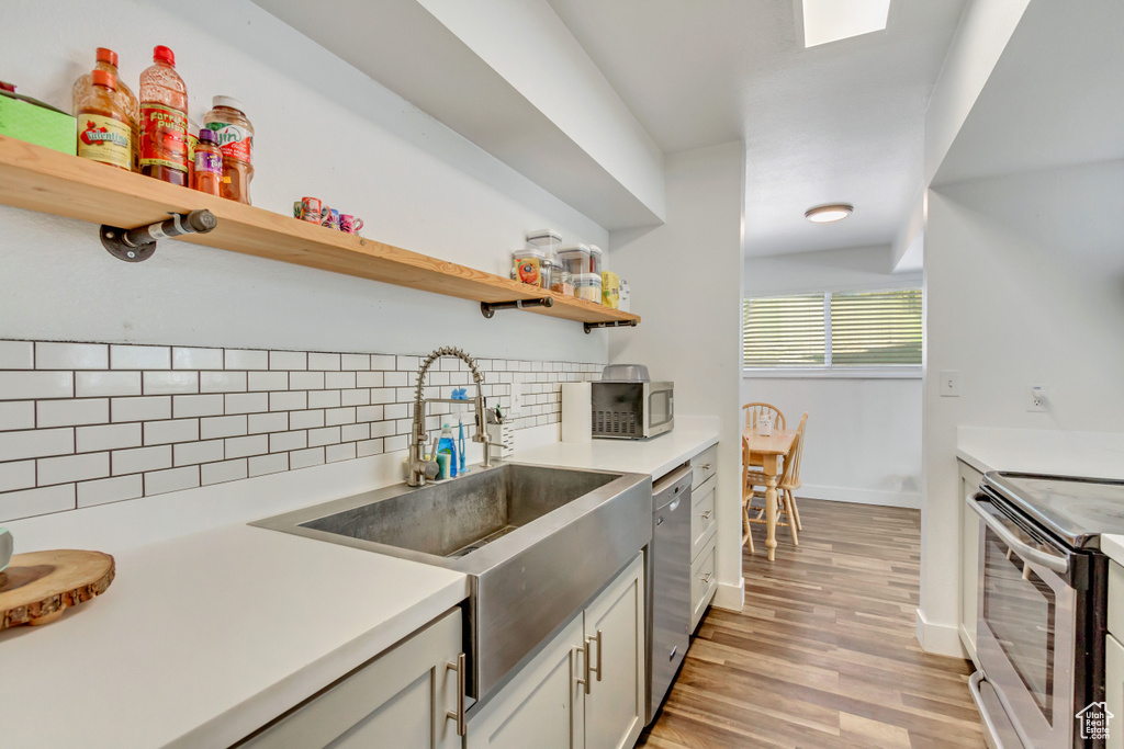 Kitchen with sink, backsplash, white cabinetry, appliances with stainless steel finishes, and light wood-type flooring