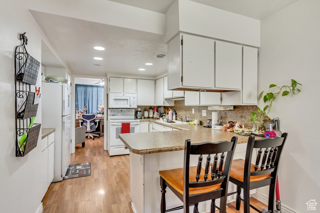 Kitchen featuring light hardwood / wood-style floors, white cabinets, backsplash, white appliances, and kitchen peninsula