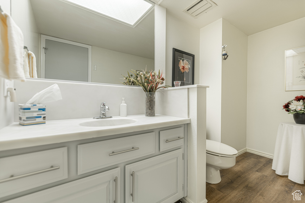 Bathroom with a skylight, vanity, toilet, and hardwood / wood-style flooring