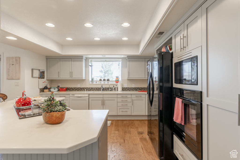 Kitchen with light hardwood / wood-style flooring, black appliances, gray cabinetry, and sink