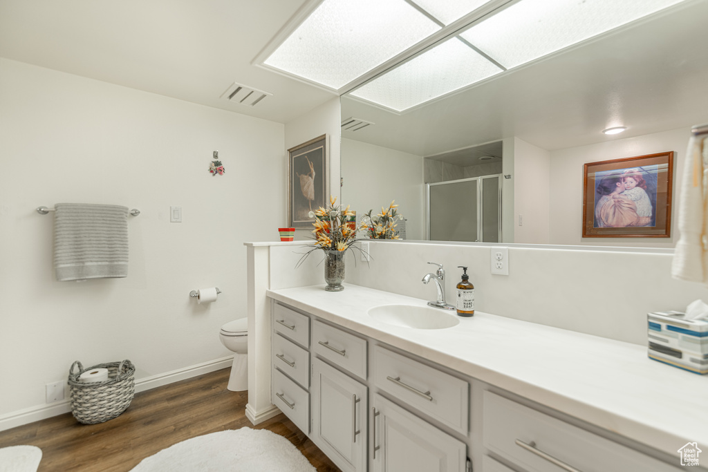 Bathroom featuring walk in shower, hardwood / wood-style floors, vanity, and toilet