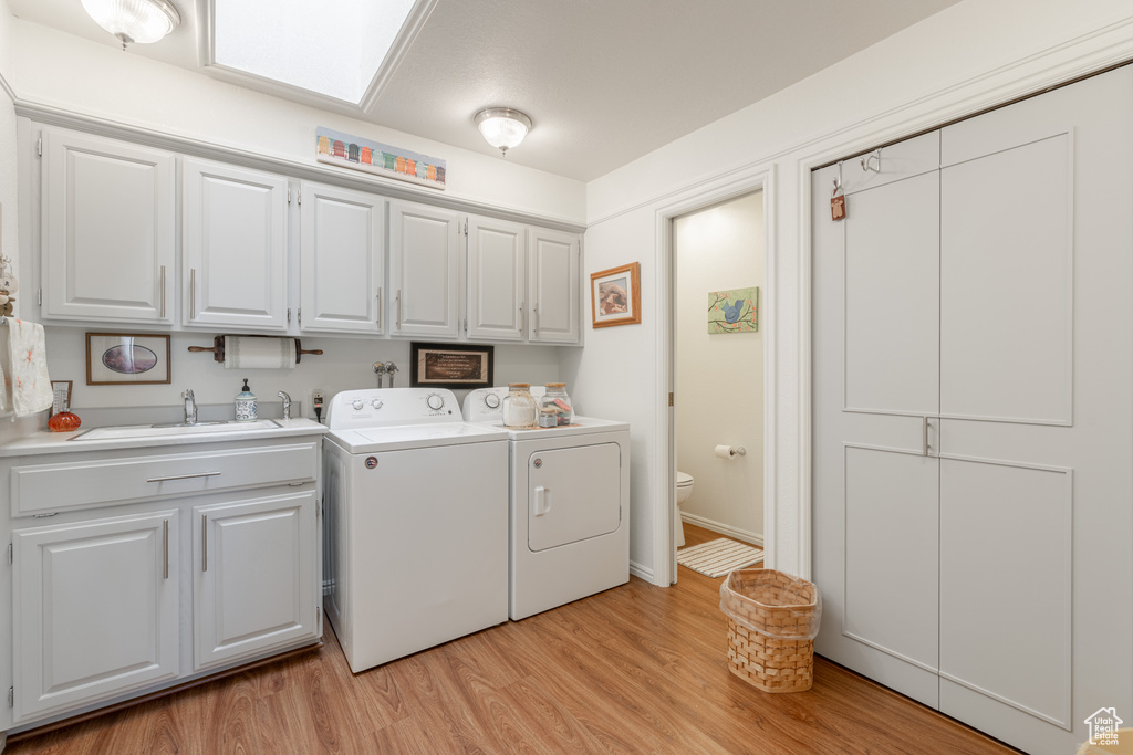 Clothes washing area with light hardwood / wood-style floors, a skylight, cabinets, sink, and washing machine and clothes dryer