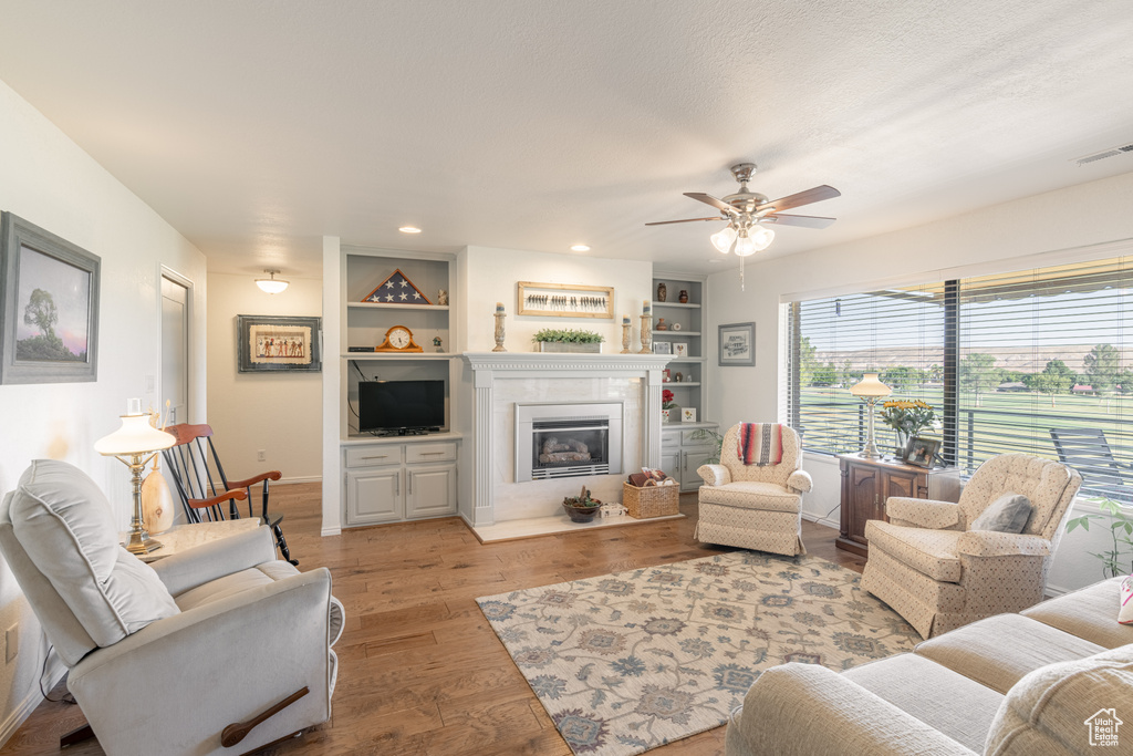 Living room with built in shelves, ceiling fan, and light hardwood / wood-style flooring