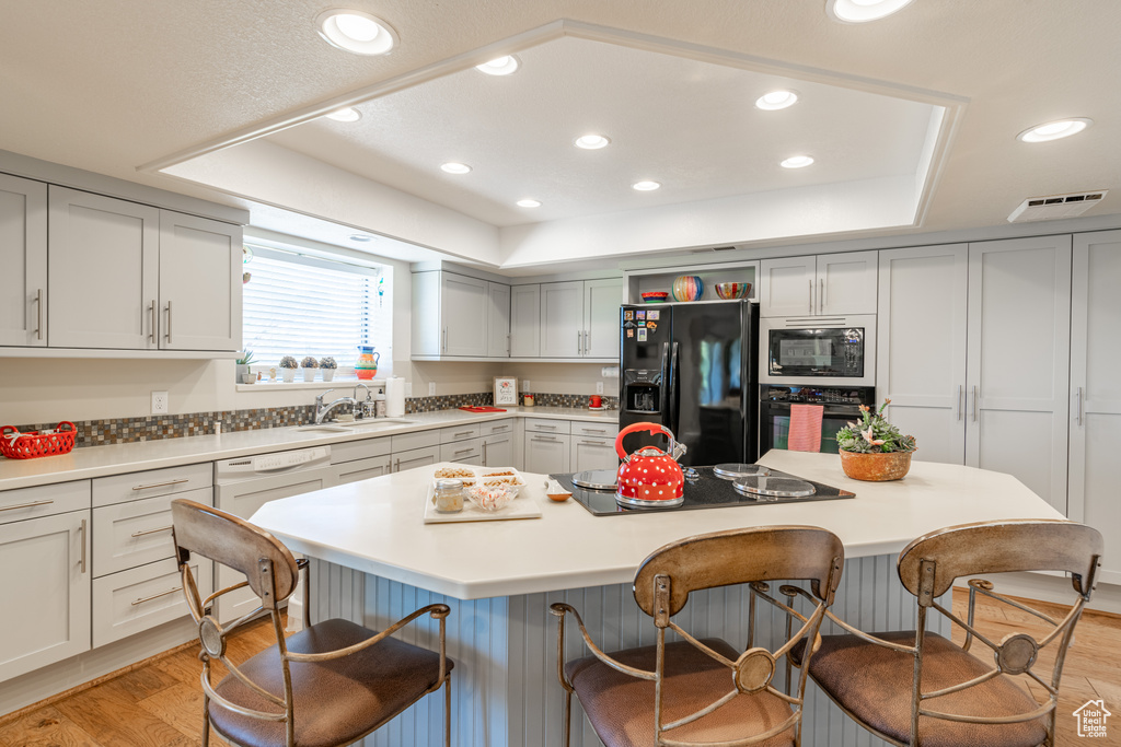 Kitchen with light hardwood / wood-style flooring, a kitchen breakfast bar, a center island, and black appliances