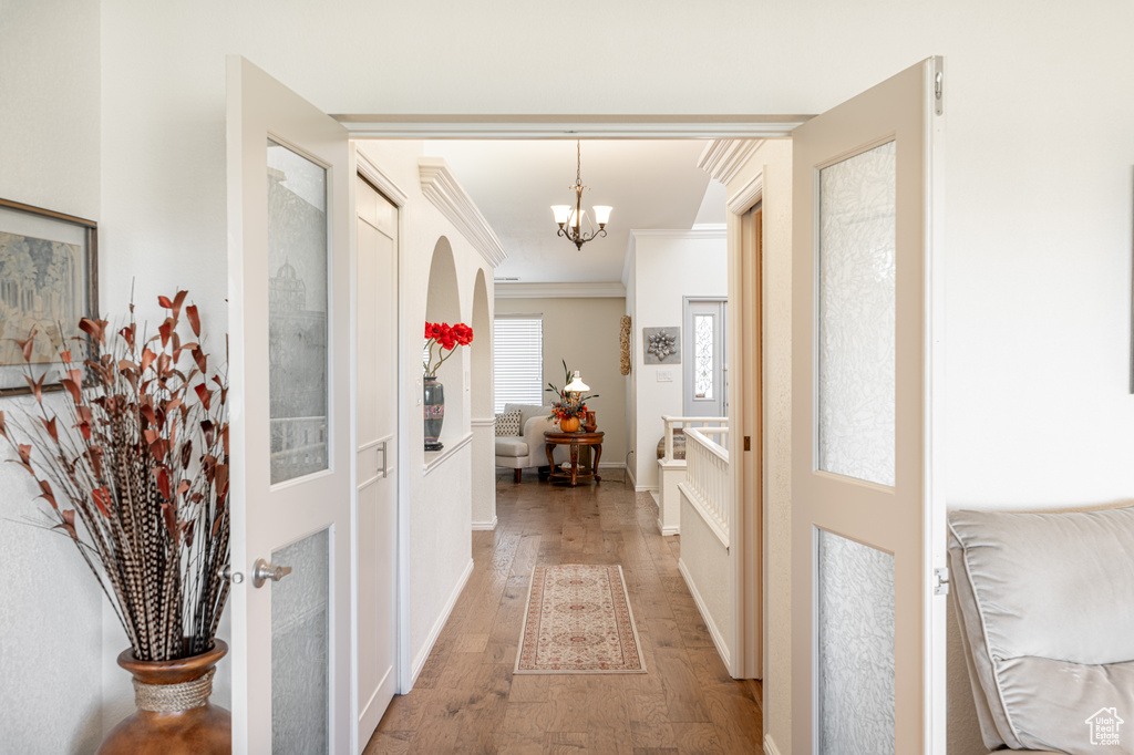 Hallway featuring ornamental molding, an inviting chandelier, and hardwood / wood-style flooring