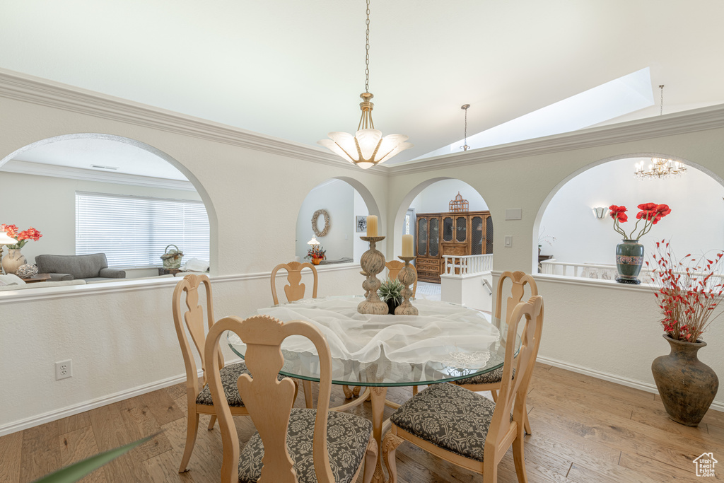 Dining space featuring crown molding, lofted ceiling with skylight, light hardwood / wood-style flooring, and a notable chandelier