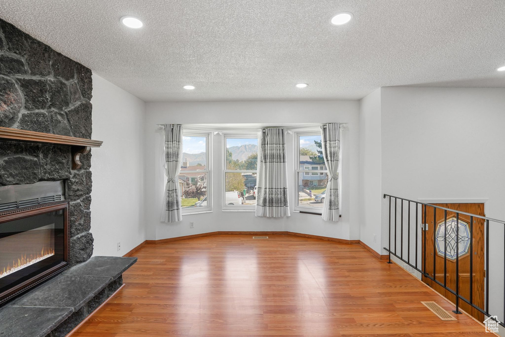 Unfurnished living room with hardwood / wood-style flooring, a fireplace, and a textured ceiling