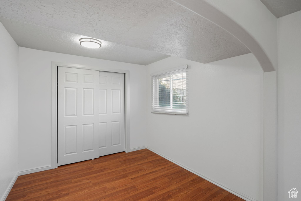 Unfurnished bedroom with a textured ceiling, a closet, and hardwood / wood-style floors