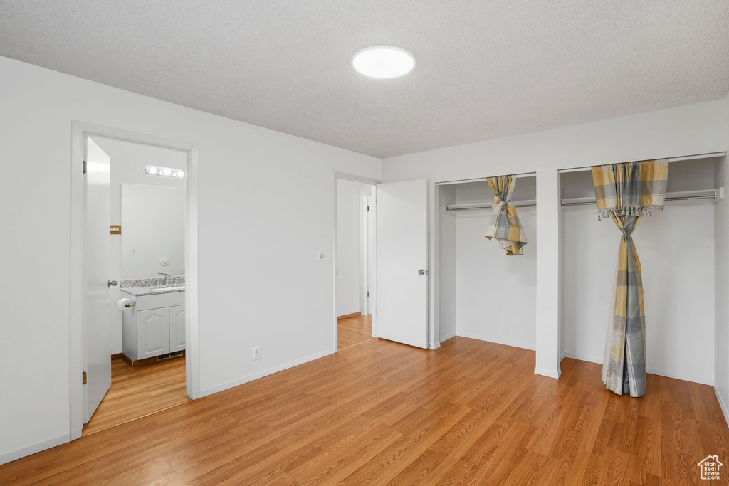 Unfurnished bedroom featuring light hardwood / wood-style flooring, multiple closets, a textured ceiling, and ensuite bathroom