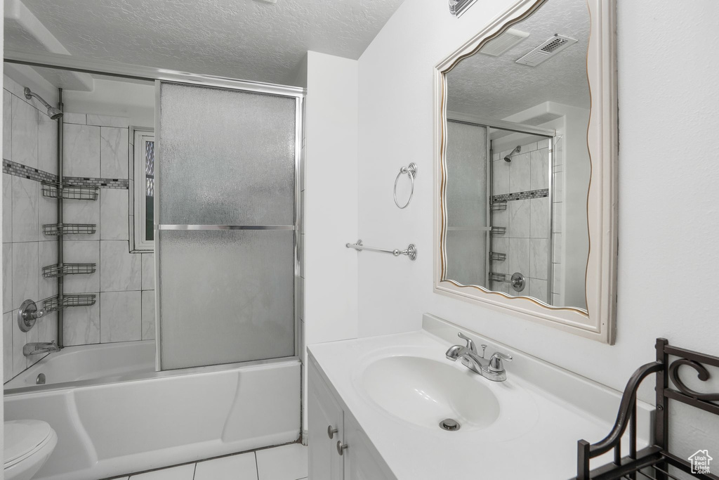 Full bathroom featuring enclosed tub / shower combo, vanity, toilet, a textured ceiling, and tile patterned flooring