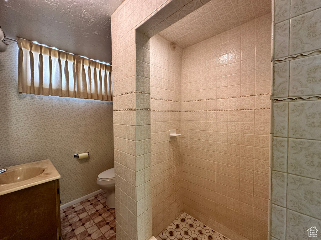 Bathroom featuring a tile shower, vanity, and toilet