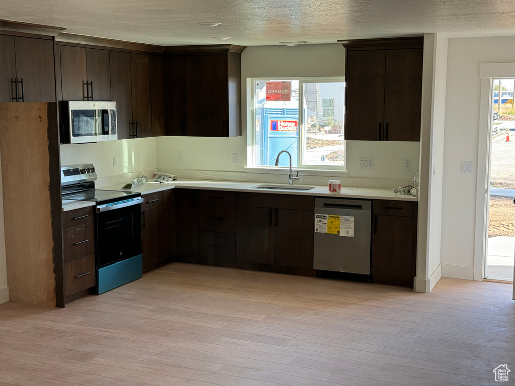 Kitchen with dark brown cabinets, stainless steel appliances, light wood-type flooring, and sink