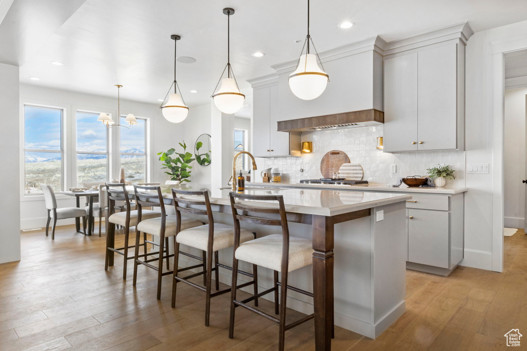 Kitchen with hanging light fixtures, decorative backsplash, custom range hood, and a center island with sink