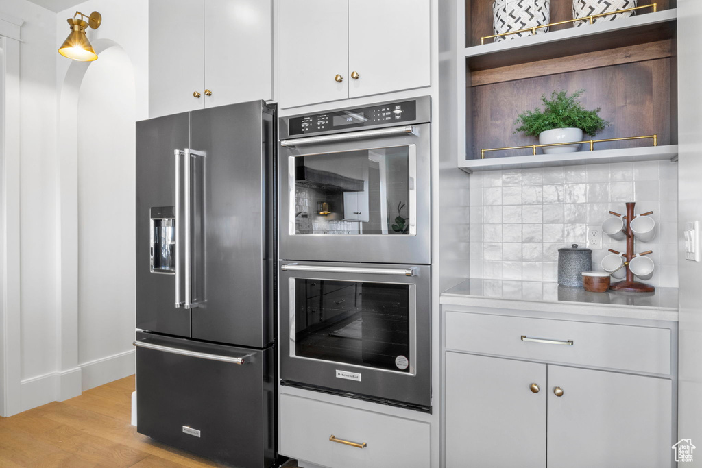 Kitchen featuring white cabinetry, stainless steel appliances, light hardwood / wood-style flooring, and backsplash