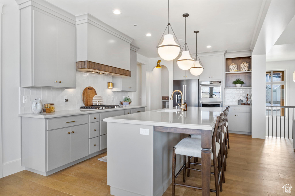 Kitchen with hanging light fixtures, light hardwood / wood-style flooring, a kitchen breakfast bar, stainless steel appliances, and a kitchen island with sink