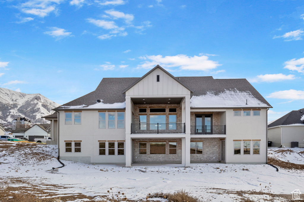 Snow covered back of property featuring a mountain view and a balcony