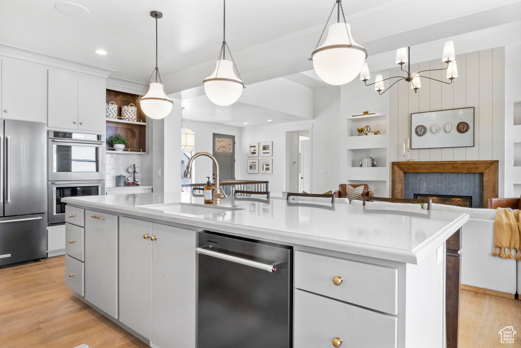 Kitchen featuring pendant lighting, sink, stainless steel appliances, an island with sink, and white cabinets