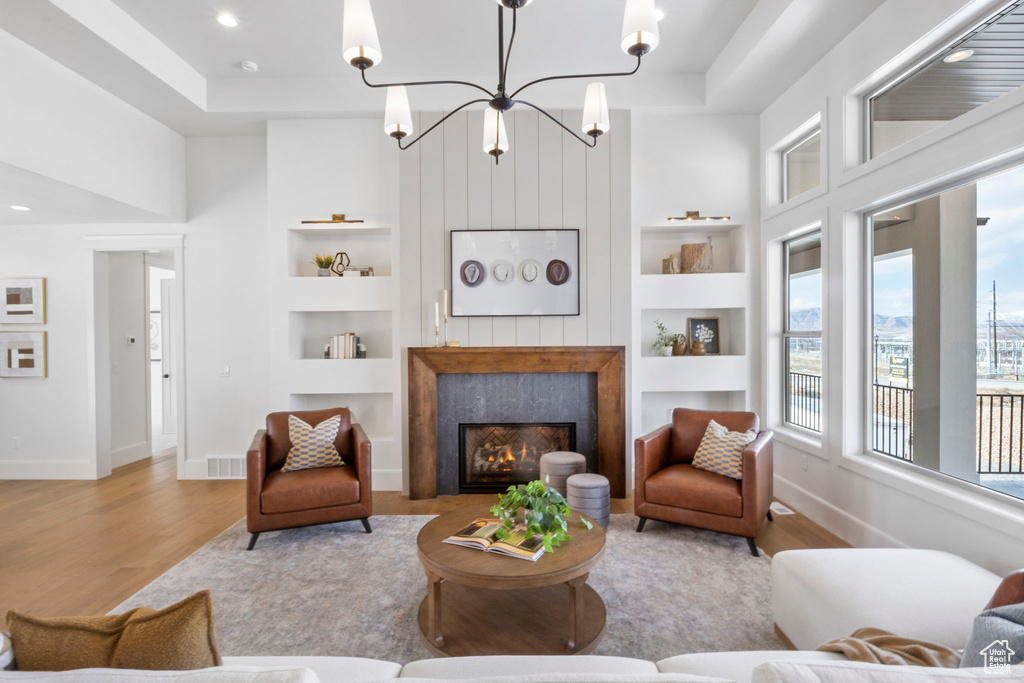 Living room featuring a raised ceiling, built in features, and light wood-type flooring