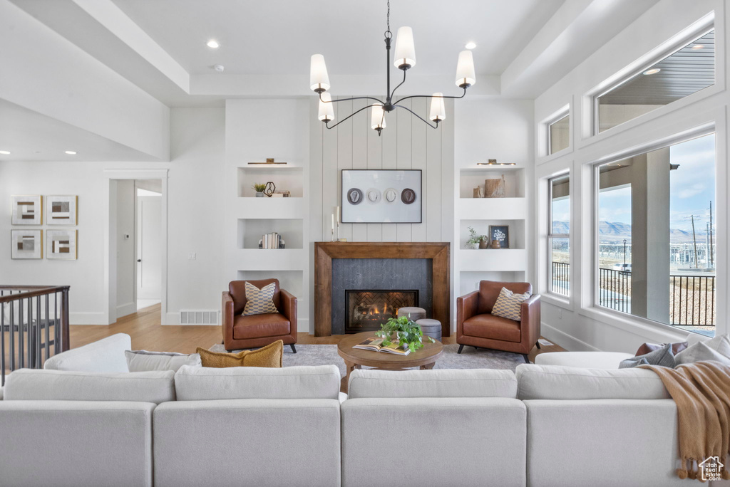 Living room featuring light hardwood / wood-style flooring, a high end fireplace, built in features, and a raised ceiling