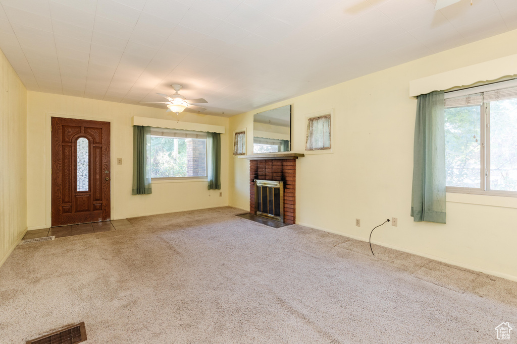 Unfurnished living room featuring a brick fireplace, ceiling fan, carpet floors, and a healthy amount of sunlight